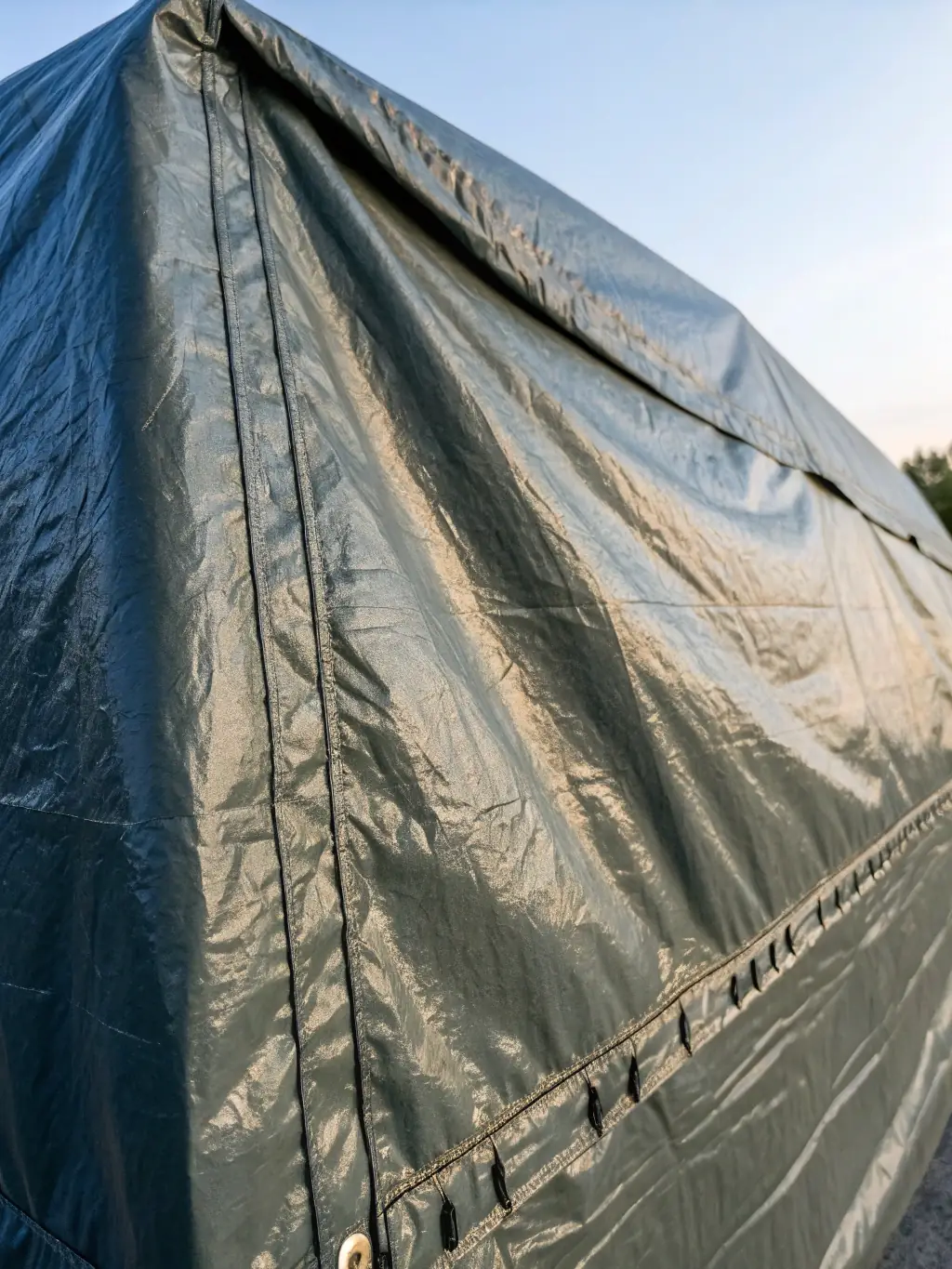 A close-up shot of a silver HDPE tarpaulin stretched over a greenhouse frame, demonstrating its strength and UV resistance in an agricultural setting.
