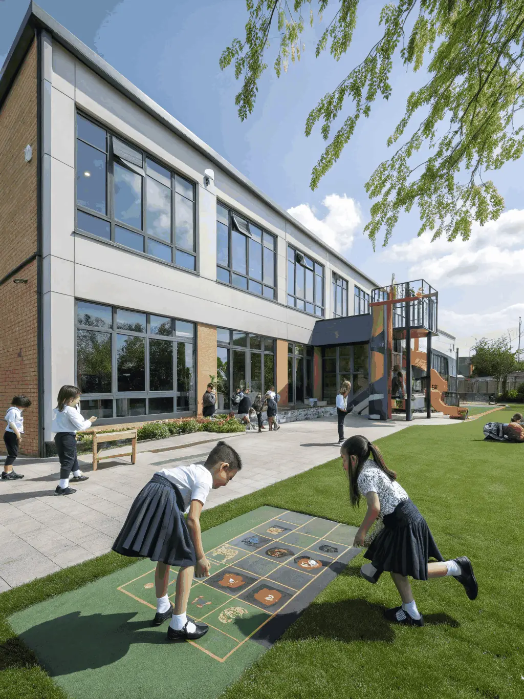 A school playground with bird netting above open corridors and seating areas, children playing safely below, showing a secure educational environment.